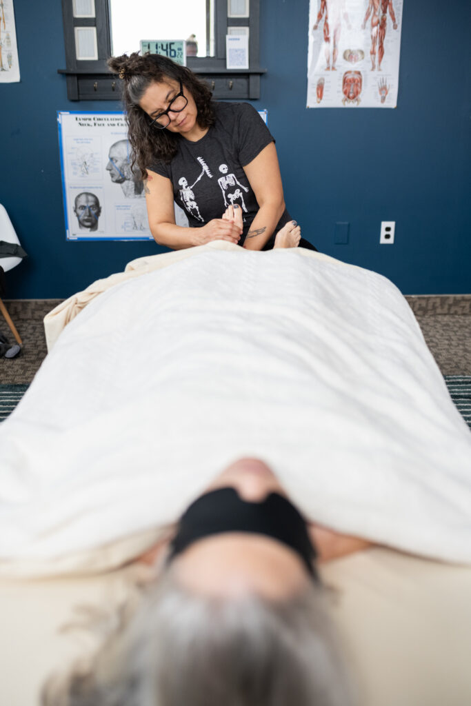 Person laying on massage table with licensed massage therapist working on feet